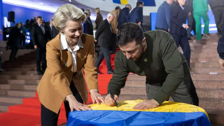 Wolodymyr Selenskyj und Ursula von der Leyen schreiben ihre Wünsche auf eine ukrainische Flagge. (Foto: Uncredited/Ukrainian Presidential Press Office/AP/dpa)
