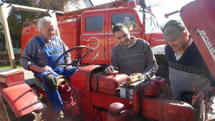 Wolfgang Schmotzer (rechts) überprüft mit seinem Team einen alten Traktor. Im Hintergrund ist ein 65 Jahre altes, funktionsfähiges Feuerwehrauto zu sehen. (Foto: Ernst Werner Schneider)