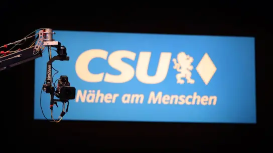 Eine Kamera hängt vor einem CSU-Logo. (Foto: Karl-Josef Hildenbrand/dpa/Archivbild)