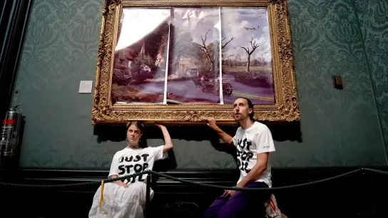 Klimaaktivisten der Organisation Just Stop Oil haben ihre Hände an den Rahmen des Gemäldes „The Hay Wain“ von John Constable geklebt, das sie zunächst mit einer auf Poster gedruckten dystopischen Version des Bildes verkleidet hatten. (Foto: Kirsty O'connor/PA Wire/dpa)