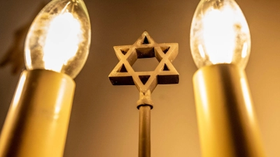 Ein siebenarmiger Leuchter (Menora) mit einem Davidstern in der Mitte leuchtet in einer Synagoge. Fragen zum Judentum werden auf einer Website beantwortet. (Foto: David Inderlied/dpa)