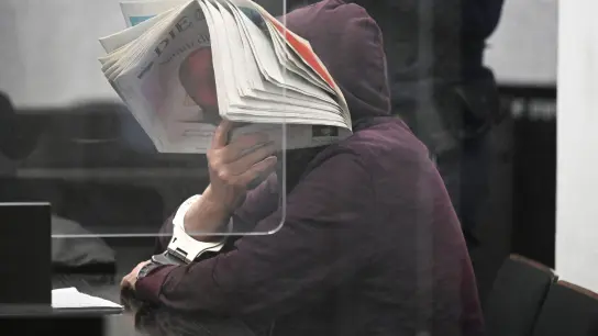 Der Angeklagte versteckt sein Gesicht hinter einer Zeitung. (Foto: Bernd Weißbrod/dpa)