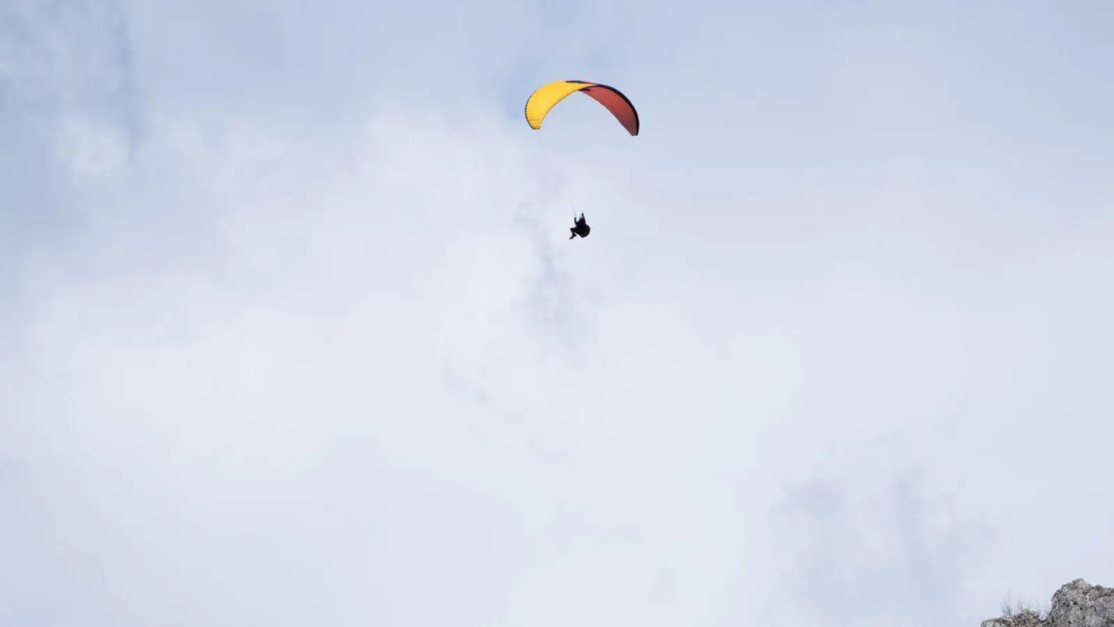 Ein Paraglider fliegt bei teilweise blauem Himmel an einem Berg vorbei. (Foto: Nicolas Armer/dpa)