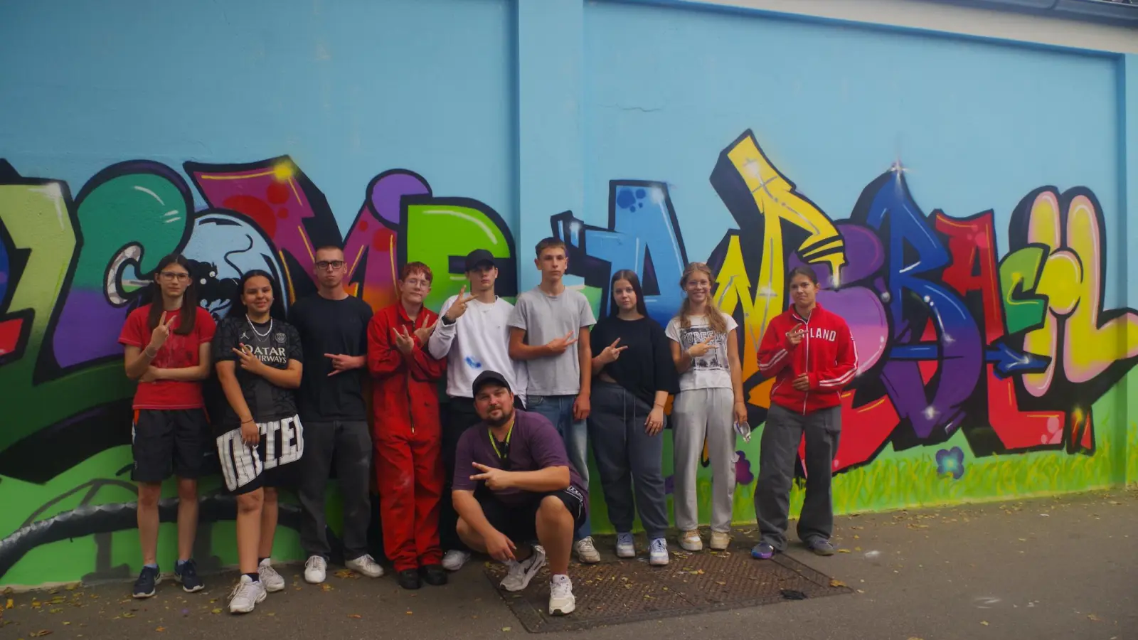 Marco Holzinger (kniend) und die Jugendlichen präsentieren ihren neuen Graffiti-Gruß. Sheima Bouzid vom Jugendrat war als Unterstützung dabei (Zweite von links). (Foto: Jannic Hofmuth)