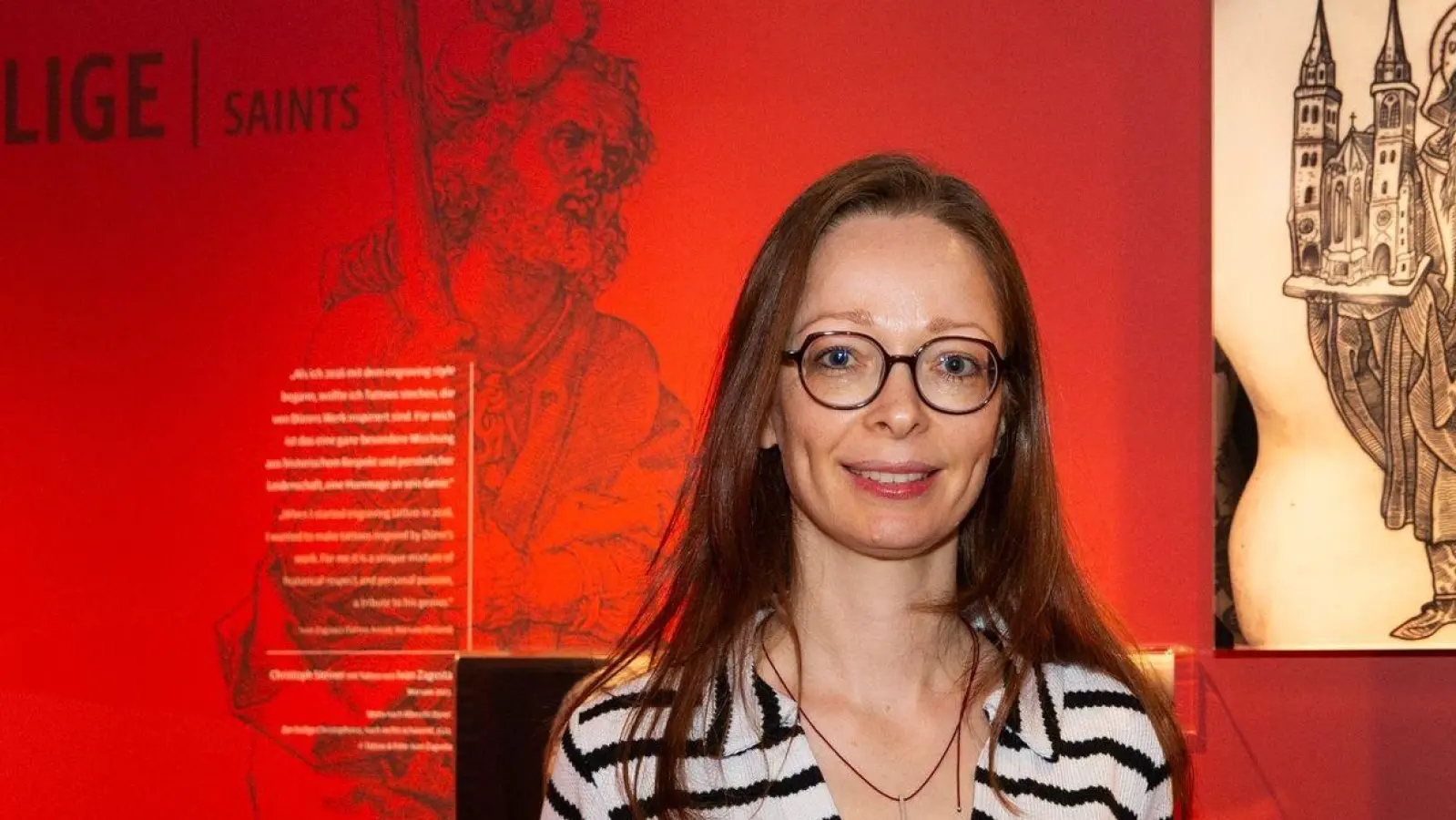 Die Museumsleiterin und Kuratorin Christine Demele steht vor einer Ausstellungstafel mit Fotografien von Tätowierungen, die nach Kunstwerken von Albrecht Dürer entstanden sind. (Foto: Oliver Frank/Albrecht-Dürer-Haus/dpa)