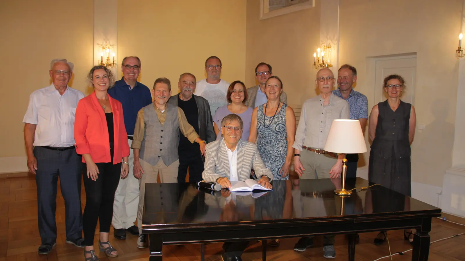Ulrich Rach (sitzend) hat für das Buch „Vorwiegend heiter“ etliche Autoren um sich versammelt. Ein Teil von ihnen hat bei der Buchvorstellung in der Karlshalle auch etwas vorzutragen. Mit im Bild sind Musikerin Ulrike Koch (r.) und alle an der Entstehung des Buches Beteiligten. (Foto: Robert Maurer)
