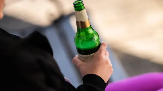 Eine Jugendliche sitzt mit einer Flasche Bier auf einer Parkbank. (Foto: Silas Stein/dpa/Illustration)