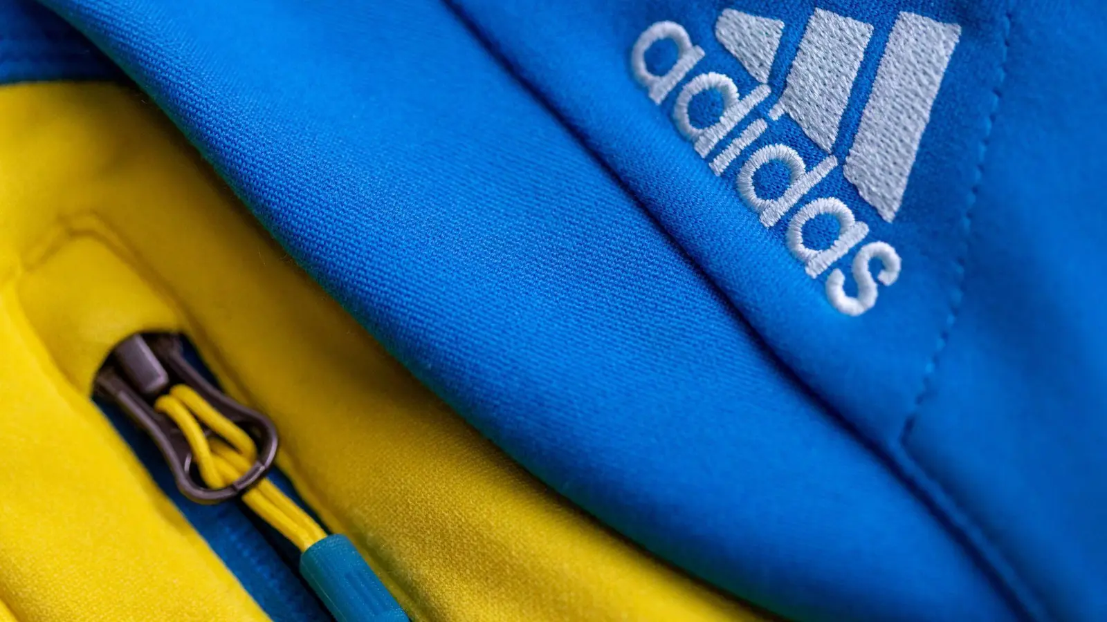 Das Logo des Sportartikelherstellers adidas auf einer blau-gelben Jacke. (Foto: Daniel Karmann/dpa/Symbolbild)