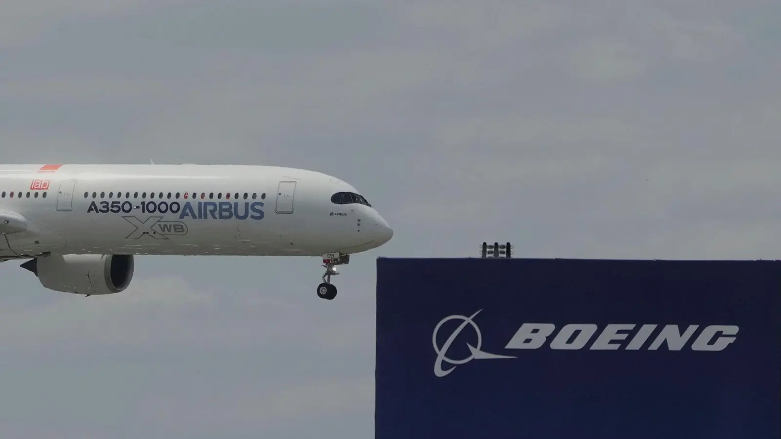 Die zwei großen Konkurrenten: Ein Airbus fliegt bei einer Vorführung auf der Luftfahrtmesse Salon du Bourget an einem Logo von Boeing vorbei. (Foto: Michel Euler/AP/dpa)