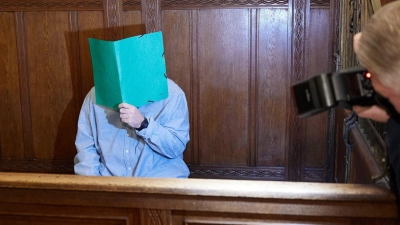 Der Angklagte sitzt im Landgericht Berlin und verbirgt sein Gesicht hinter einem Schnellhefter. (Foto: Joerg Carstensen/dpa)