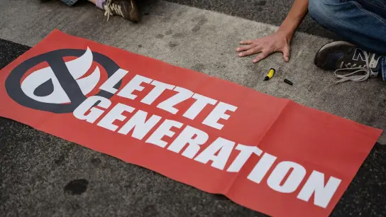 Aktivisten der Gruppe „Letzte Generation“ haben sich hinter einem Banner mit ihrem Logo festgeklebt. (Foto: Swen Pförtner/dpa/Symbolbild)