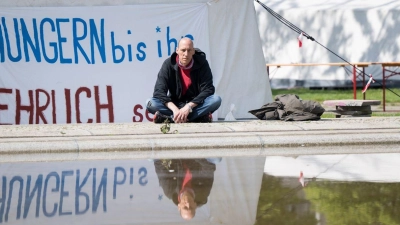 Wolfgang Metzeler-Kick sitzt am neuen Standort des Hungerstreik-Camps des Bündnisses „Hungern bis ihr ehrlich seid“ im Regierungsviertel vor einem Banner. (Foto: Sebastian Gollnow/dpa)