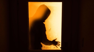 Der Schatten eines Mannes ist hinter einer gläsernen Wohnungstür zu sehen. (Foto: Nicolas Armer/dpa/Illustration)