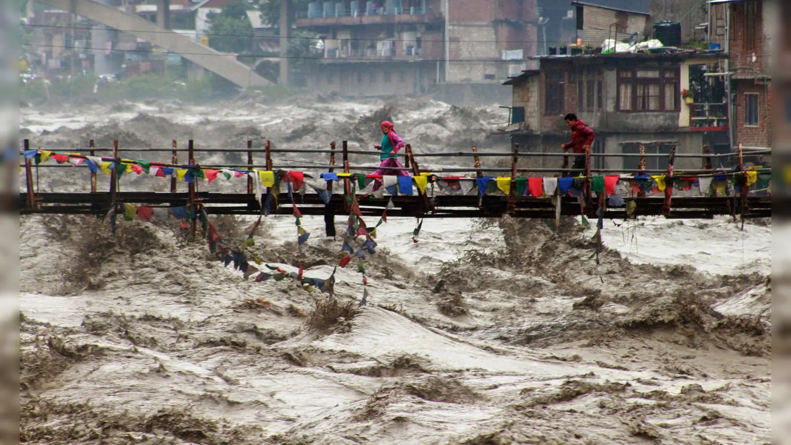 Menschen wagen im nordindischen Bundesstaat Himachal Pradesh trotz schwerer Überschwemmungen den Weg über eine Brücke, um den Fluss Beas zu überqueren. (Foto: Aqil Khan/AP/dpa)