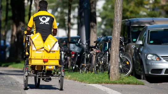 Ein Briefträger fäht mit seinem Fahrrad eine Straße in München entlang. (Foto: Sven Hoppe/dpa/Symbolbild)