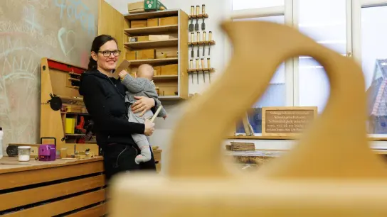 Johanna Röh steht mit ihrem Kind auf dem Arm in der Werkstatt ihres Betriebes. Die Mutter und Tischlermeisterin hat eine Petition zur Reform des Mutterschutzes auf den Weg gebracht. (Foto: Friso Gentsch/dpa)