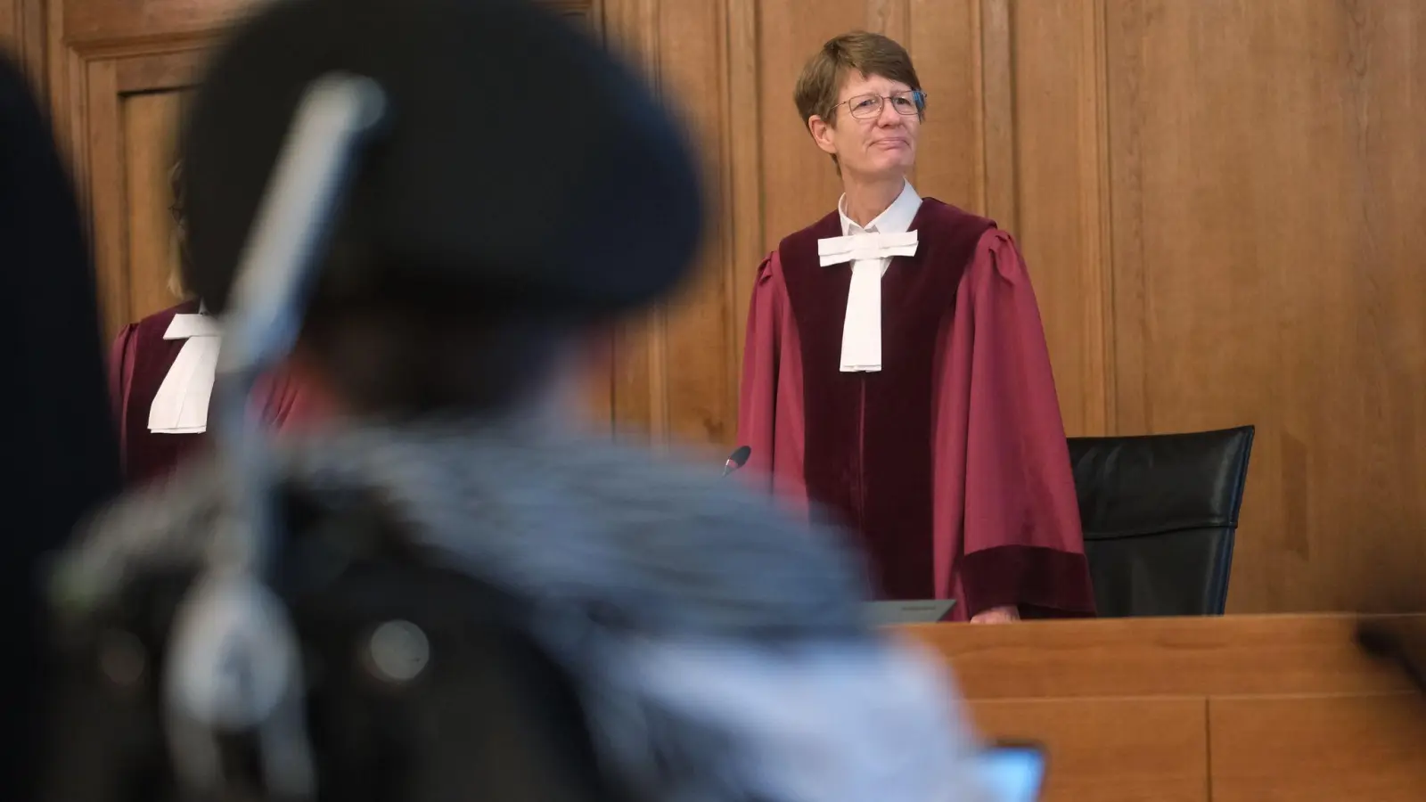 Renate Philipp, Versitzende Richterin am Bundesverwaltungsgericht, steht während der Verhandlung im Gerichtssaal in Leipzig. Im Vordergrund sitzt einer Kläger im Rollstuhl. (Foto: Sebastian Willnow/dpa)