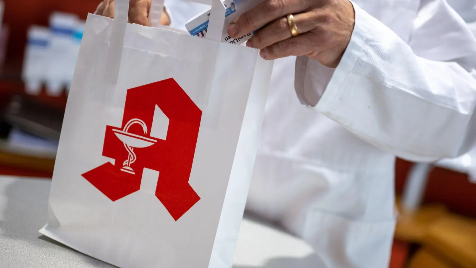 Ein Apotheker legt in einer Apotheke eine Packung mit Tabletten in eine Papiertasche mit Apotheken-Logo. (Foto: Monika Skolimowska/dpa)