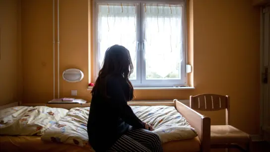 Eine Frau sitzt in einem Frauenhaus auf einem Bett. (Foto: Maja Hitij/dpa)