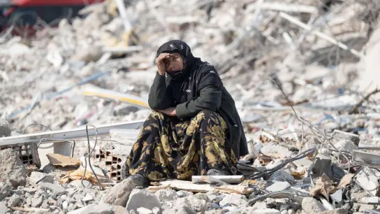Eine Frau in Antakya beobachtet zwischen den Trümmern die Bergung von Opfern. (Foto: Boris Roessler/dpa)