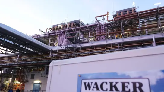 Eine Schautafel mit der Aufschrift „Wacker“ steht vor einer Anlage auf dem Gelände der Wacker Chemie. (Foto: Sebastian Willnow/dpa/Archivbild)