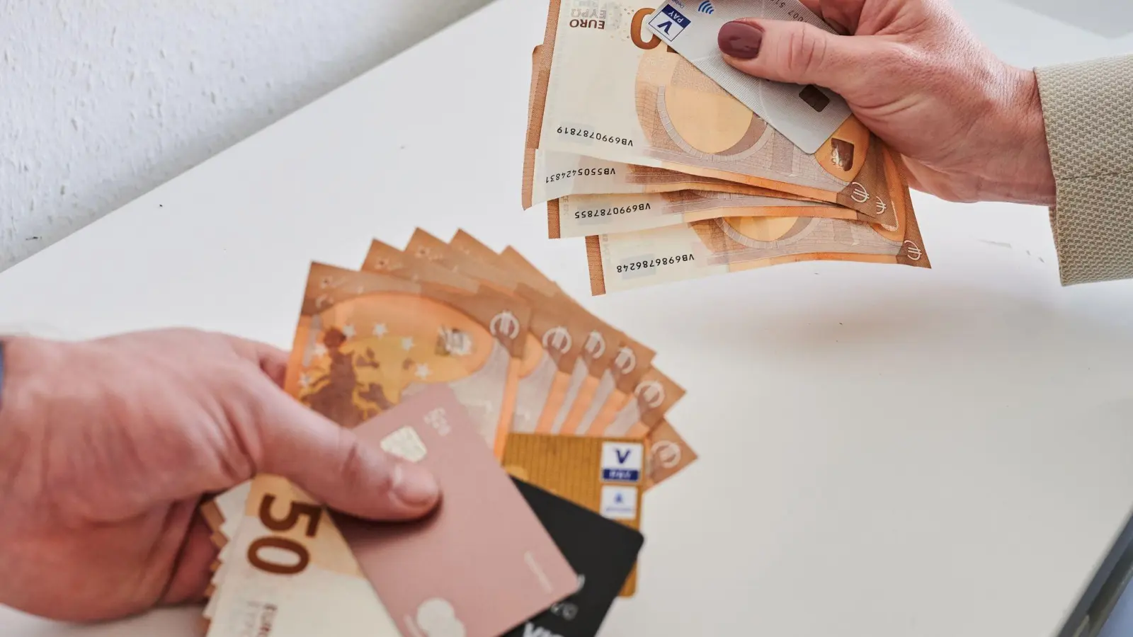 Ein Mann (l) und eine Frau halten unterschiedlich viele Geldscheine und Karten in der Hand. (Foto: Annette Riedl/dpa/Illustration)
