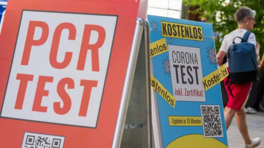 Schilder mit der Aufschrift „PCR Test“ und „Corona-Test - Kostenlos“ hängen vor dem Eingang einer Apotheke in der Innenstadt von München. (Foto: Peter Kneffel/dpa)