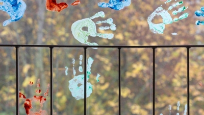 Kinder haben in einem Kindergarten farbige Abdrücke ihrer Hände auf einem Fenster hinterlassen. (Foto: Michael Reichel/dpa-Zentralbild/dpa)