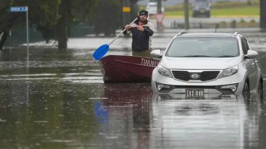Ein Mann paddelt mit seinem Boot auf einer überfluteten Straße am Stadtrand von Sydney. (Foto: Mark Baker/AP/dpa)