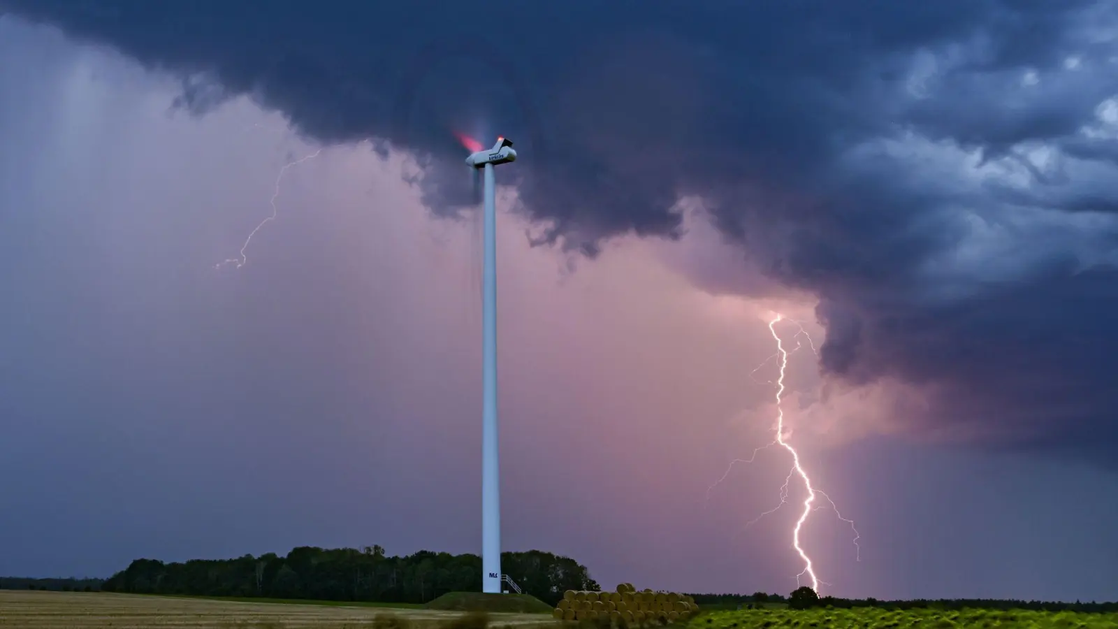 Ein Blitz leuchtet am Abendhimmel hinter einer Windenergieanlage im Osten Brandenburgs. (Foto: Patrick Pleul/dpa)