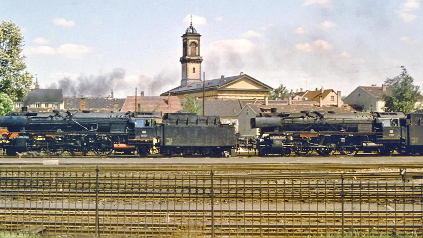 Am Ende der Dampf-Ära: Zwei Lokomotiven der Baureihe 01 Mitte der 1960er-Jahre am Bahnhof in Ansbach – im Hintergrund die katholische Kirche St. Ludwig. (Foto: Siegfried Tappert)