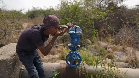 In Indien trinkt ein Mann Wasser aus einer undichten Wasserstelle. (Foto: Mahesh Kumar A./AP)