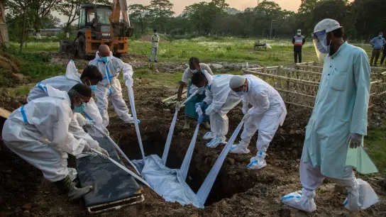 Angehörige und städtische Mitarbeiter in Schutzanzügen begraben in Indien den Körper einer Person, die an Covid-19 gestorben ist. (Foto: Anupam Nath/AP/dpa)