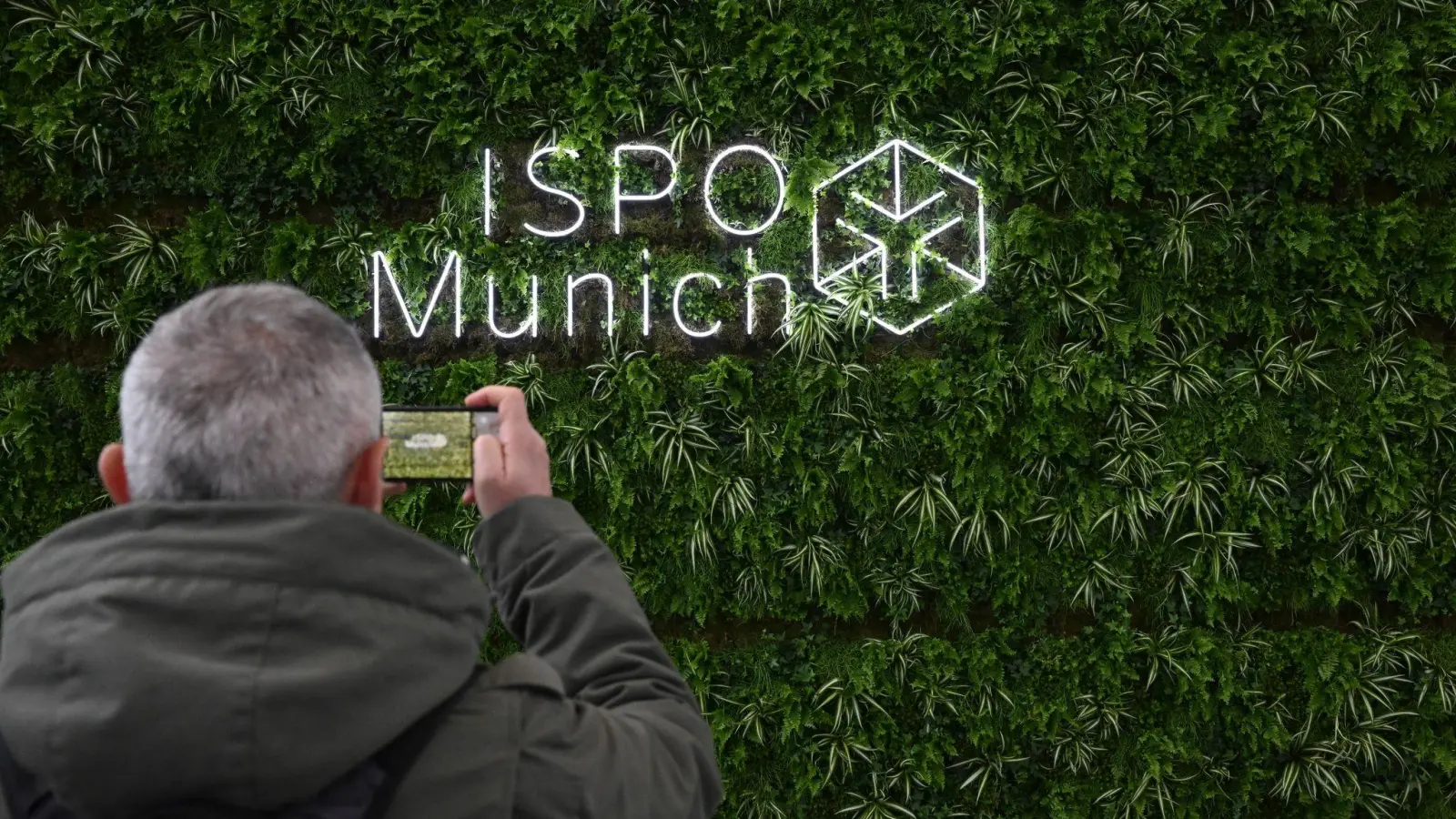 Ein Besucher fotografiert das Logo der Sportartikelmesse Ispo in der Eingangshalle der Messe München. (Foto: Felix Hörhager/dpa)