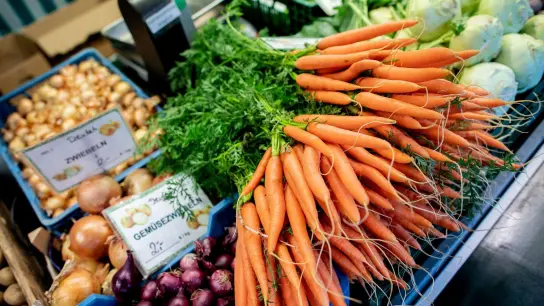 Karotten und Zwiebeln stehen an einem Obst- und Gemüsestand auf einem Wochenmarkt zum Verkauf. (Foto: Hauke-Christian Dittrich/dpa)