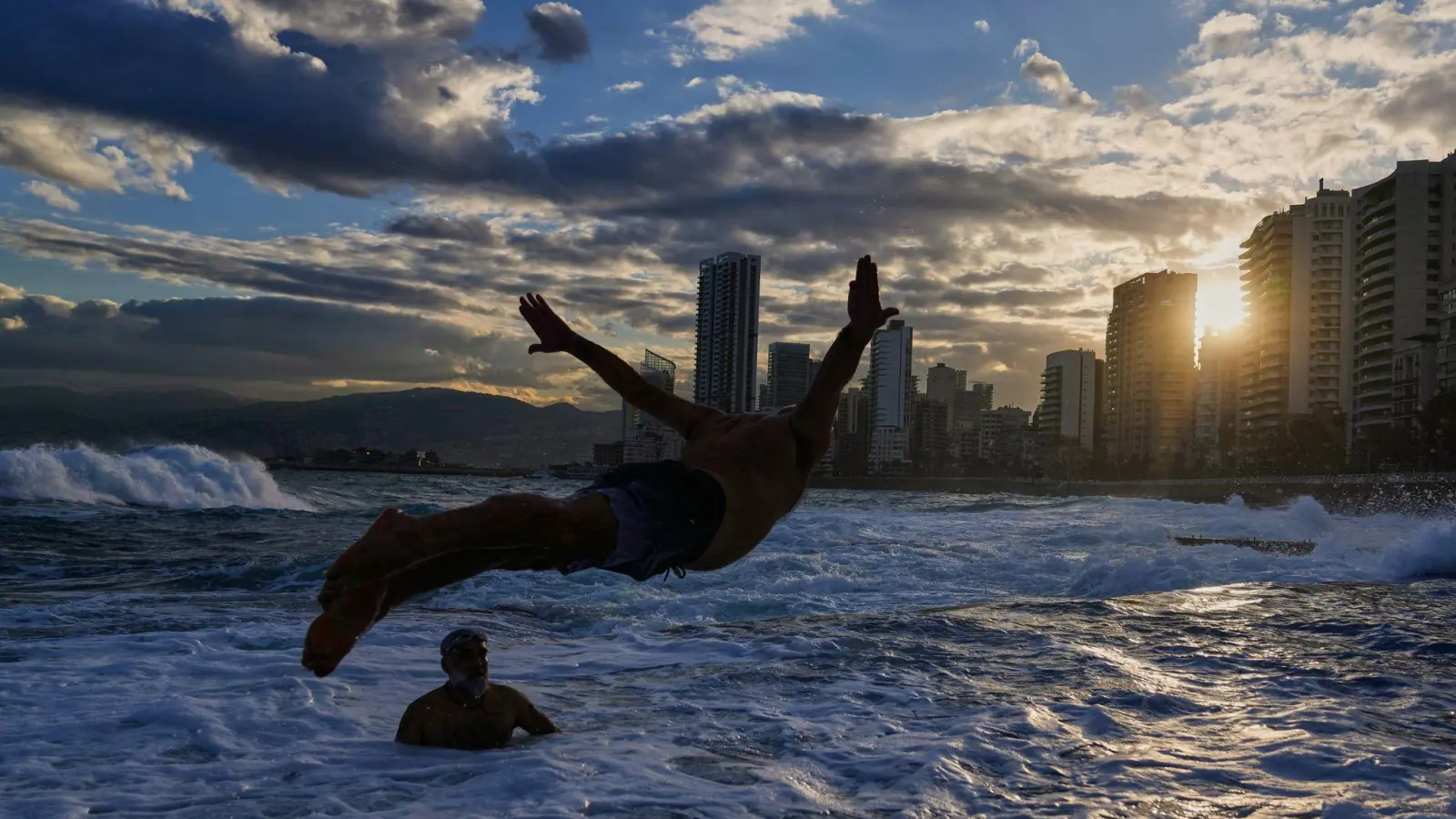Ein Mann springt bei Temperaturen um die 10 Grad Celsius ins Mittelmeer, während die Sonne über Beirut aufgeht. (Foto: Hassan Ammar/AP/dpa)