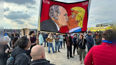 Demonstranten halten bei einer Kundgebung des Bündnisses „Eine Million Augenblicke für Demokratie“ ein Banner, auf dem sich stilisiert US-Präsident Trump und Russlands Präsident Putin küssen. (Foto: Michael Heitmann/dpa)