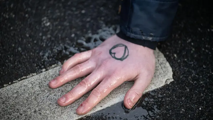 Ein Klimaaktivist hat sich mit der Hand auf den Asphalt geklebt. (Foto: Bernd Thissen/dpa/Archivbild)
