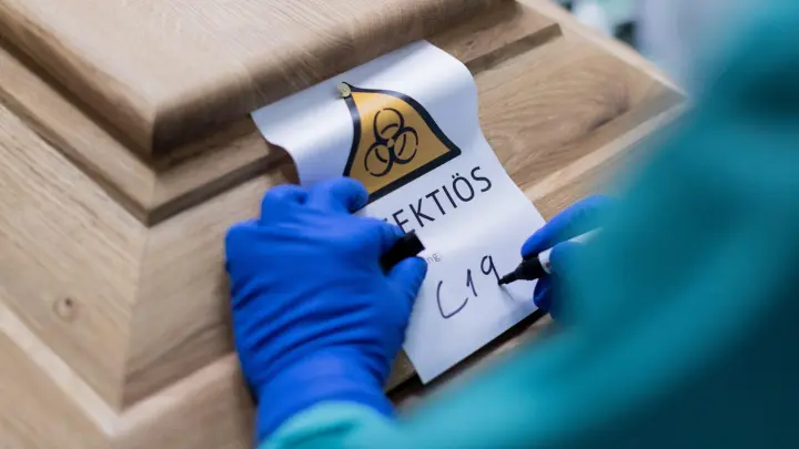 Ein Bestattungsunternehmer schreibt „C19“ auf ein Schild mit dem Hinweis „Infektiös“ auf einen Sarg mit einem Verstorbenen, der an dem Coronavirus gestorben ist. (Foto: Rolf Vennenbernd/dpa)