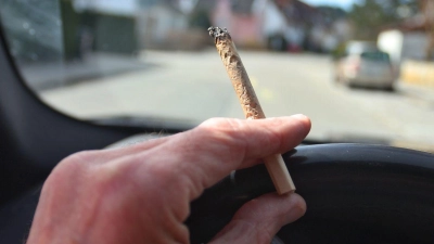 Ein Mann sitzt mit einem Joint zwischen den Fingern am Steuer eines Autos. (Foto: Karl-Josef Hildenbrand/dpa)