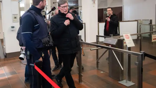 Kardinal Rainer Maria Woelki wird im Foyer des Kölner Landgerichts von einem Justizbeamten (l) zur Sicherheitsschleuse begleitet. (Foto: Marius Becker/dpa)