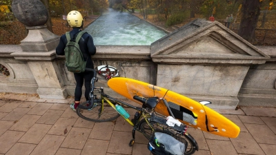 Ein Mann mit einem Surfboard an seinem Fahrrad schaut von einer Brücke auf die - nicht mehr vorhandene - Eisbachwelle im Englischen Garten. (Foto: Peter Kneffel/dpa)