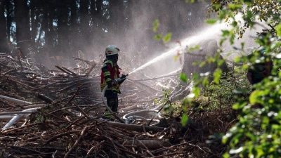 Eine Einsatzkraft der Feuerwehr löscht den Waldboden. (Foto: Daniel Vogl/dpa)