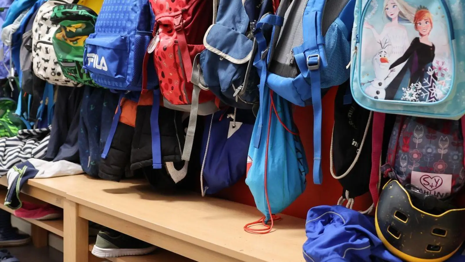 Sporttaschen und Schulranzen hängen an der Garderobe vor einem Klassenzimmer. (Foto: Christian Charisius/dpa/Symbolbild)
