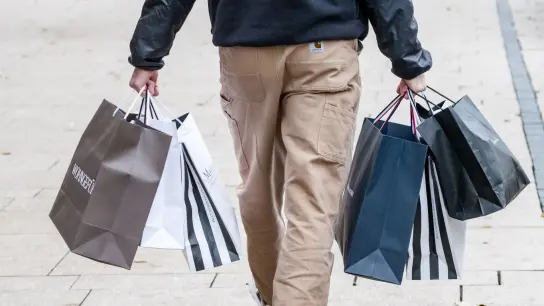 Ein Mann geht mit Einkaufstüten durch die Innenstadt. (Foto: Markus Scholz/dpa/Symbolbild)
