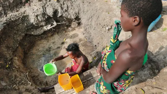 Eine Frau schöpft in Mosambik Wasser aus einer ungeschützten Quelle. (Foto: Tsvangirayi Mukwazhi/AP/dpa)