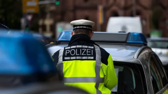 Ein Polizeibeamter steht zwischen zwei Einsatzfahrzeugen der Polizei. (Foto: Philipp von Ditfurth/dpa/Symbolbild)