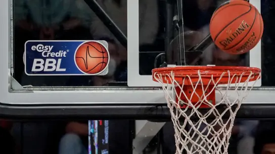 Ein Ball fliegt auf den Korb zu, an dem ein Logo der Basketball-Bundesliga klebt. (Foto: Axel Heimken/dpa/Symbolbild)