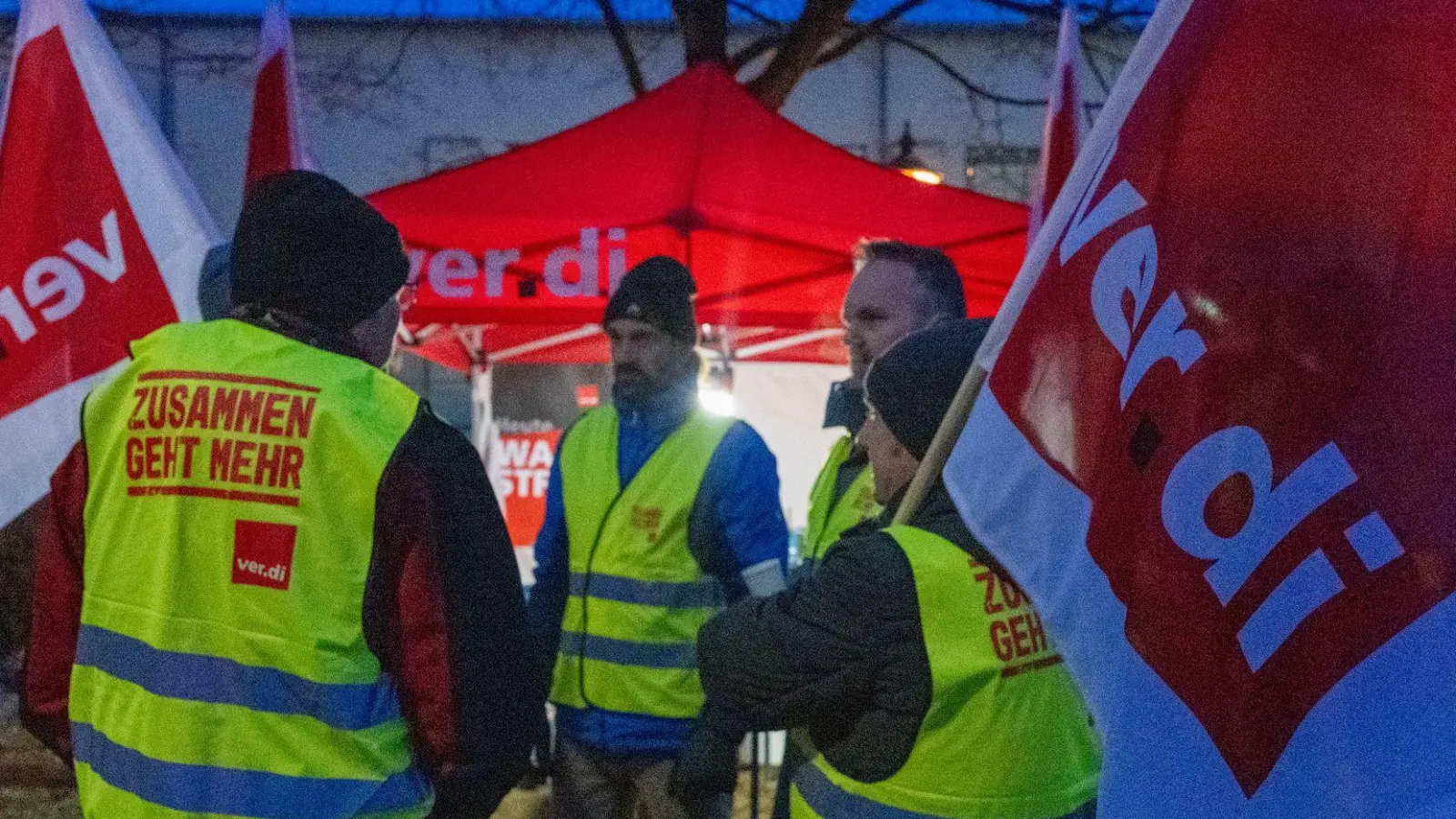 Streikende halten Fahnen der Gewerkschaft Verdi und sind mit Warnwesten gekleidet.  (Foto: Stefan Puchner/dpa)