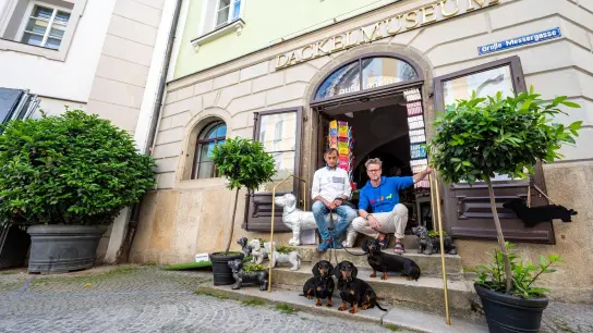 Seppi Küblbeck (l) und Oliver Storz sitzen mit ihren Dackeln vor ihrem Dackelmuseum. (Foto: Armin Weigel/dpa/Archivbild)